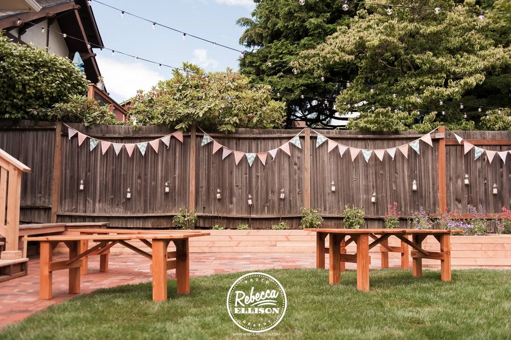 An intimate backyard wedding space is decorated with penant banners, lights and picnic tables photographed by Rebecca Ellison photography