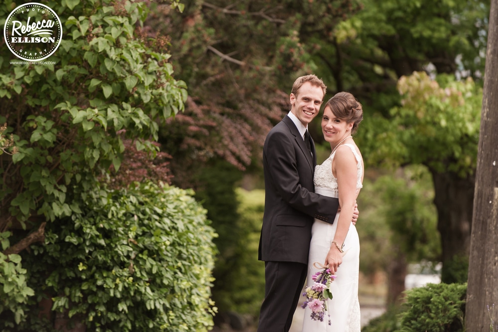 Outdoor wedding portraits featuring a lush garden and a white wedding dress with lace detail and purple flowers photographed by Rebecca Ellison Photography