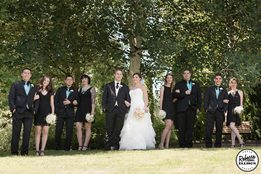 Wedding party stands under a huge oak tree featuring black bridesmaids dresses, black suits with blue vests and ties photographed by Rebecca Ellison Photography