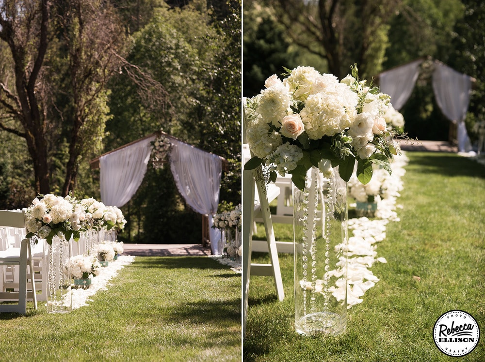 Wedding ceremony details at an outdoor garden wedding featuring a wooden arbor with billowing white curtains and clear vases lined with crystals and filled with white flowers line the aisle photographed by Seattle wedding photographer Rebecca Ellison