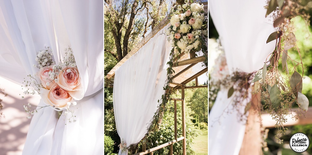 White curtains, peach roses, white flowers and leaves decorate a wooden wedding arbor at an outdoor garden wedding photographed by Seattle wedding photographer Rebecca Ellison