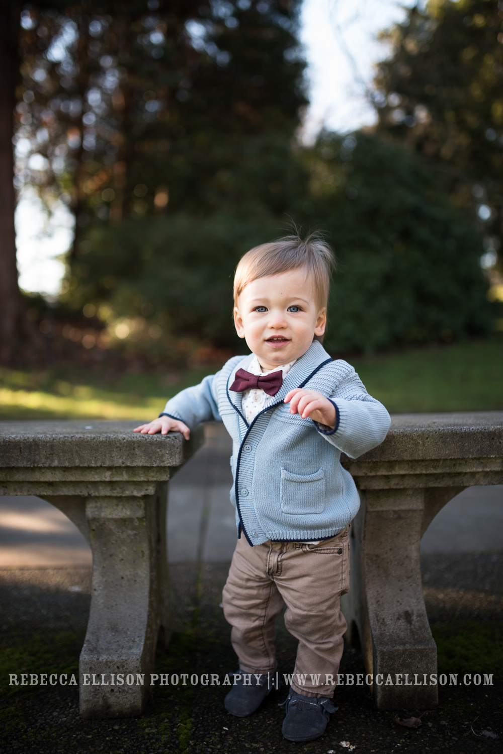 one year old stands in bow tie between benches at park