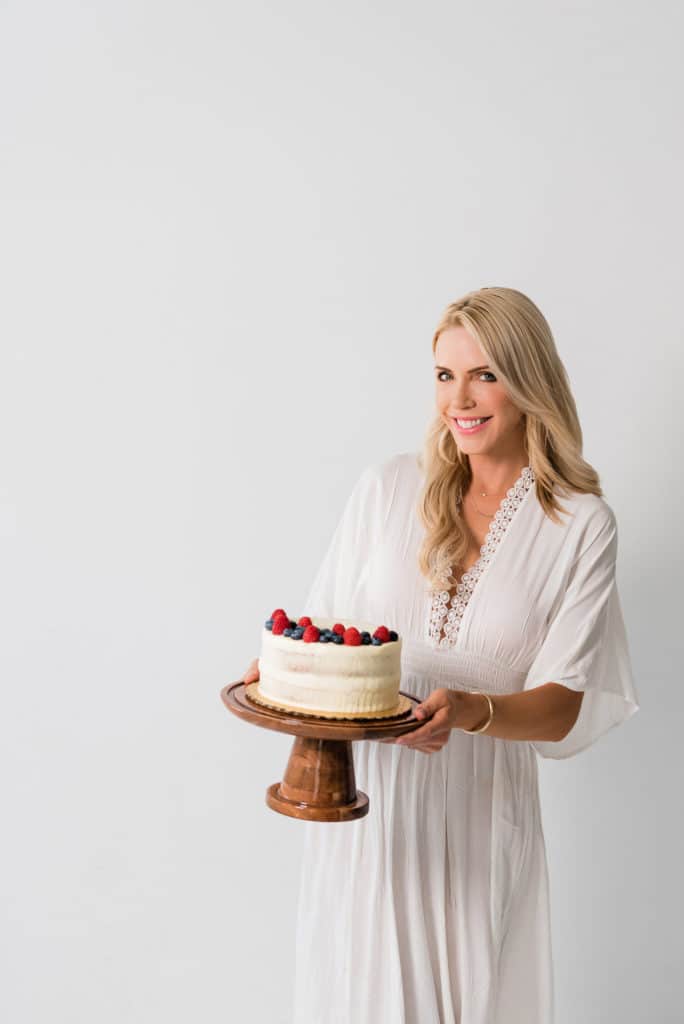 brand photoshoot of Sarah Jio wearing a white dress and holding a cake on a cake stand